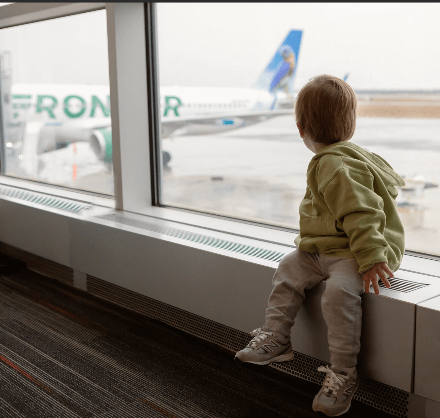 Child looking out airport window at Frontier airplane 
